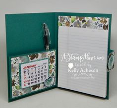 an open notebook with a calendar and pen attached to the cover, sitting on a table