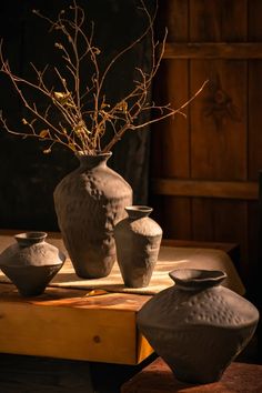 three vases sitting on top of a wooden table next to a plant in a vase