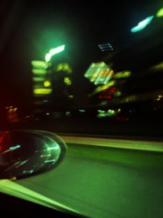 a blurry image of a car driving down the road at night with city lights in the background