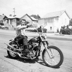 a man riding on the back of a motorcycle down a street next to small houses