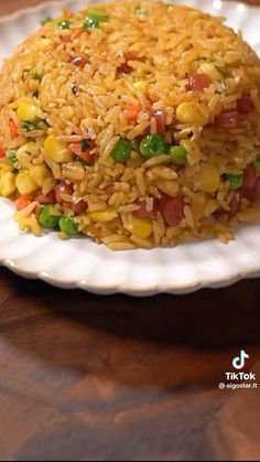 rice with peas and corn on a white plate sitting on a wooden table next to a fork