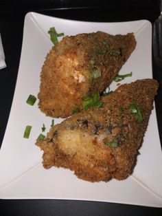 two pieces of fried food on a white plate with green onions and seasoning sprinkles