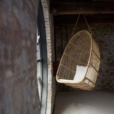 a hanging chair in the corner of a room with brick walls and exposed ceilinging