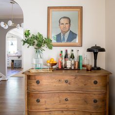 a wooden dresser topped with lots of bottles and glasses next to a painting on the wall