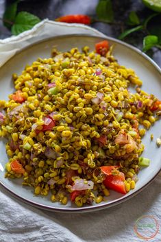 a white plate topped with corn salad next to a bowl of tomatoes and other vegetables