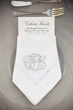 the table is set with silverware and white napkins, which are decorated with an elegant monogram