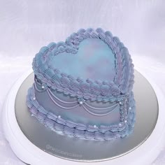 a blue heart shaped cake sitting on top of a white platter with silver trim