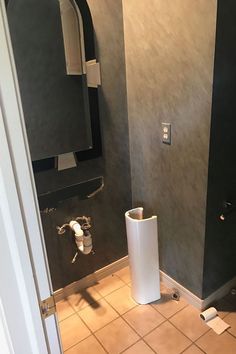 a bathroom with black walls and tile flooring, toilet paper roll holder in the corner