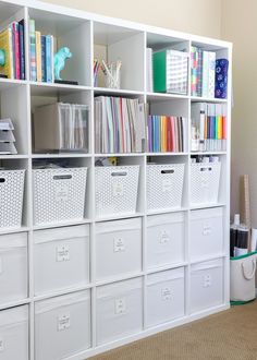 a white bookcase filled with lots of books next to a wall full of bins