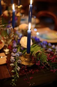 candles are lit on a table with flowers and greenery in front of the plates