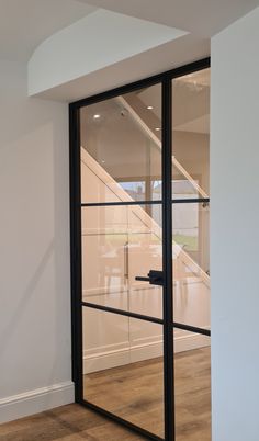 an open glass door in the middle of a room with wood flooring and white walls