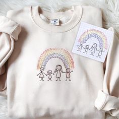 a white sweater with an image of people holding hands and a rainbow on it next to a card