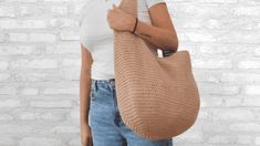 a woman holding a knitted bag in front of a brick wall