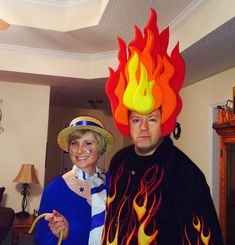 a man and woman dressed up in costumes with flames on their heads, standing next to each other