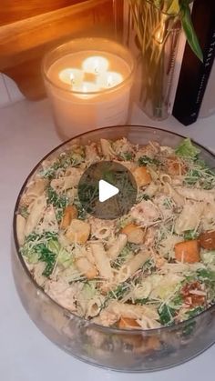 a glass bowl filled with pasta salad next to a lit candle on top of a table