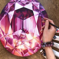 a person is painting a pink diamond on a wooden table with markers and paintbrushes