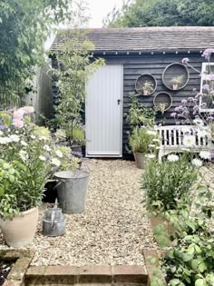 an outdoor garden with potted plants and flowers in front of a small shed that has a white door