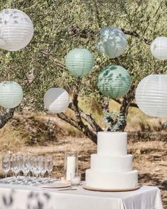 a table topped with a white cake and lots of paper lanterns hanging from the trees