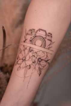 a woman's arm with a camera and flowers tattoo on the left side of her arm