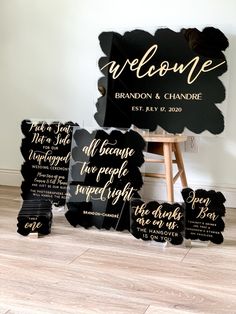 black and gold wedding welcome signs on wooden floor next to easel with chair in background