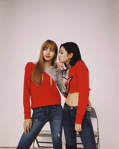 two young women standing next to each other in front of a white wall and chair