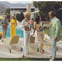 three women and two men standing near a pool talking to each other in front of some lawn chairs