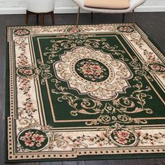 a green rug with an ornate design on the floor in front of two white chairs