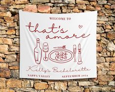 a welcome sign hanging on the side of a stone wall with wine bottles and utensils