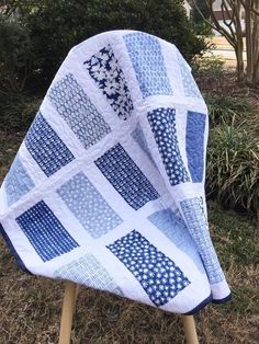 a blue and white quilt sitting on top of a wooden chair in front of some bushes