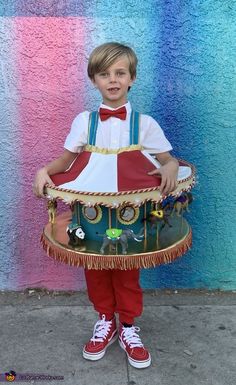 a young boy in red pants and white shirt holding a drum