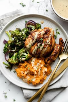 a white plate topped with chicken, mashed potatoes and broccoli next to a fork