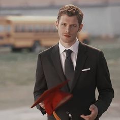 a man in a suit and tie holding a red flag next to a school bus