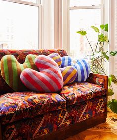 colorful pillows are on the back of a couch in front of two windows with potted plants