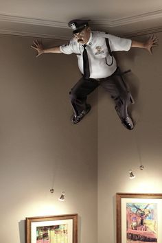 a police officer is suspended from the ceiling above two beds in a hotel room with paintings on the walls