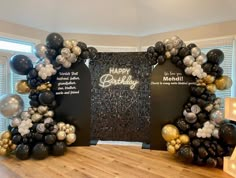 two black and gold balloons are in front of a happy birthday sign on the wall