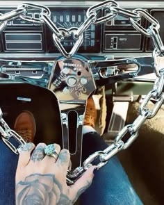 a man with tattoos on his arm is sitting in a car and has chains attached to the steering wheel