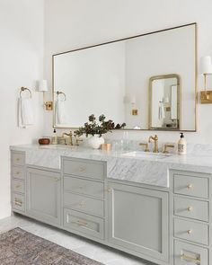 a bathroom with two sinks, mirrors and gold accents on the wall above it is an area rug