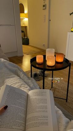 an open book sitting on top of a bed next to two candles