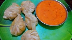 some dumplings are sitting on a green plate with a bowl of dipping sauce next to them