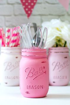 pink mason jars filled with kitchen utensils and paper straws on a table