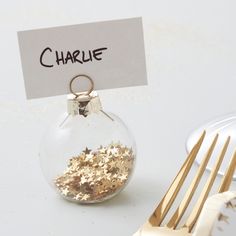 a table setting with silverware, gold forks and a glass ornament that says charlie