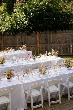 an outdoor dining table set up with white linens and floral centerpieces on it