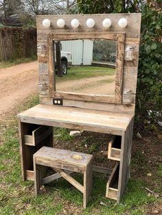 a wooden vanity with a mirror and stool in the grass next to a fenced area