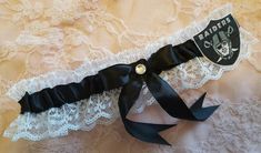 "Handcrafted wedding garter. Your choice of a single or a 2pc set. Created w/ black satin & white lace. Centered w/ black satin bow & rhinestone. To the side sits a Raiders applique. Garter stretches comfortably up to and at 22\". Please note that this product is in no way an official, licensed NFL product. I am in no way affiliated with the NFL. This is a handcrafted product, using licensed NFL material only. Larger sizes may be made to order at no additional charge. Simply leave a meas Raiders Wedding, White Lace Garter, Oakland Raiders Football, Raiders Football, Waist Cincher Corset, Wedding Garters, Personalized Ribbon, Satin Noir, Waist Training Corset