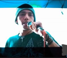 a young man singing into a microphone while wearing a beanie and green t - shirt