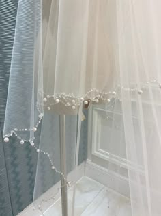 a white veil with pearls hanging from it's side next to a mirror in a room