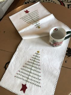 two christmas tree napkins on top of a wooden table with a coffee cup in the middle