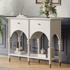 a white console table with gold legs and flowers on top, in front of a gray wall