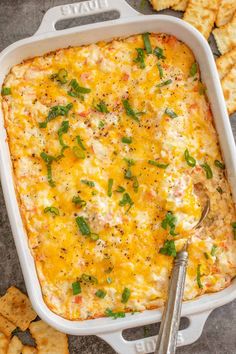 a white casserole dish with cheese and green onions in it next to crackers