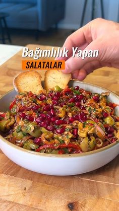 a person is dipping some bread into a bowl of food on a wooden table with the words bagmilk yapan salata above it